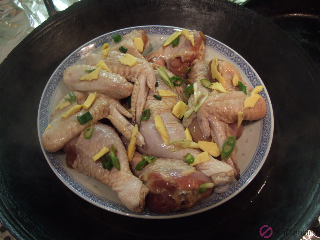 Plate of raw chicken wings, drumsticks, and leg with green onions and ginger in a wok