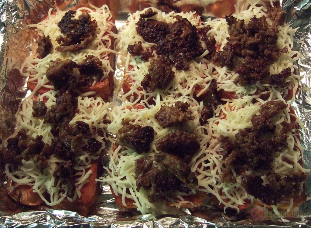 Six slices of brioche with pizza sauce, shredded mozzarella cheese, and browned Italian sausage in a baking pan