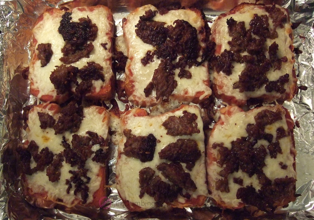 Six slices of baked Italian sausage pizza toast in a baking pan
