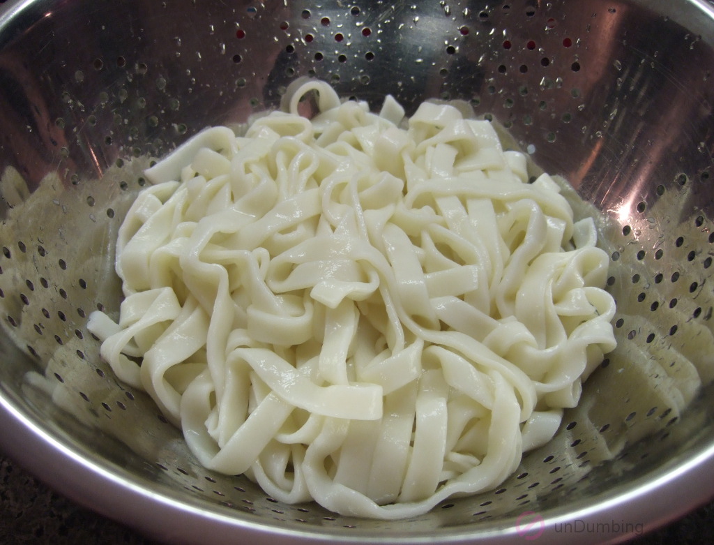 Cooked chow fun noodles in colander