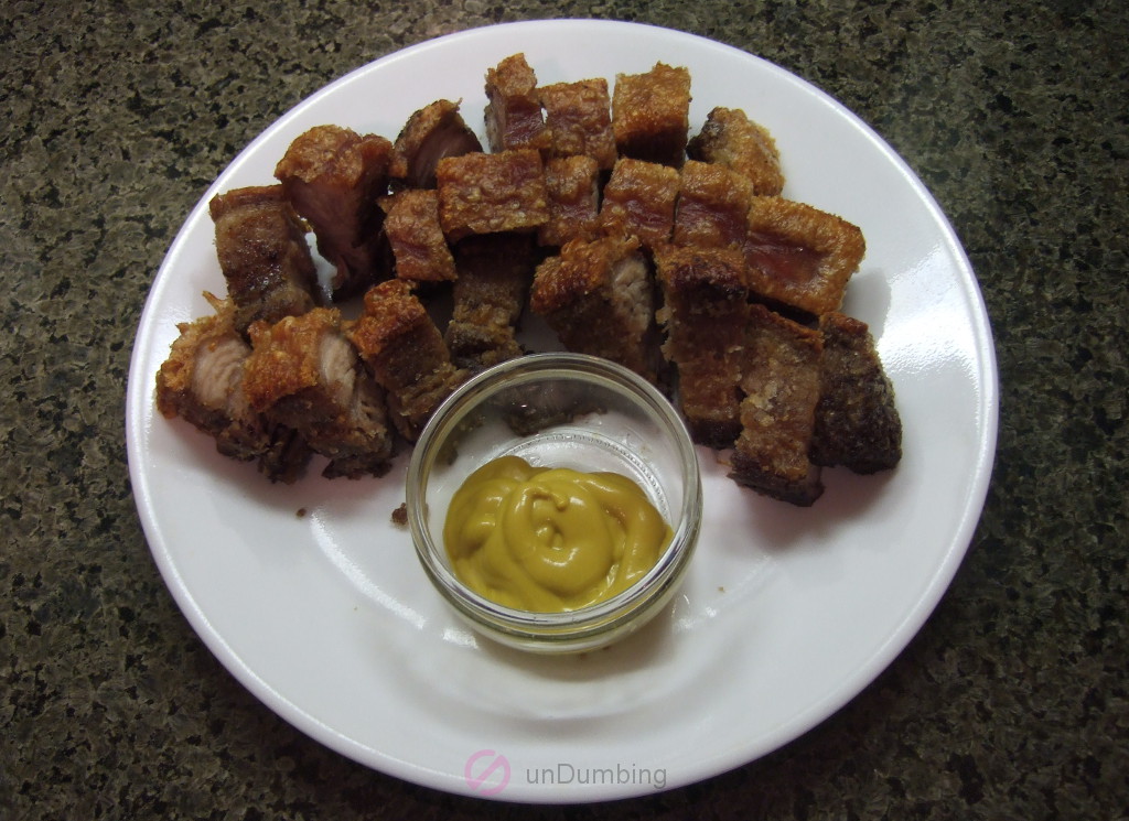 Bite-sized crispy pork belly on a white plate with a glass container of mustard