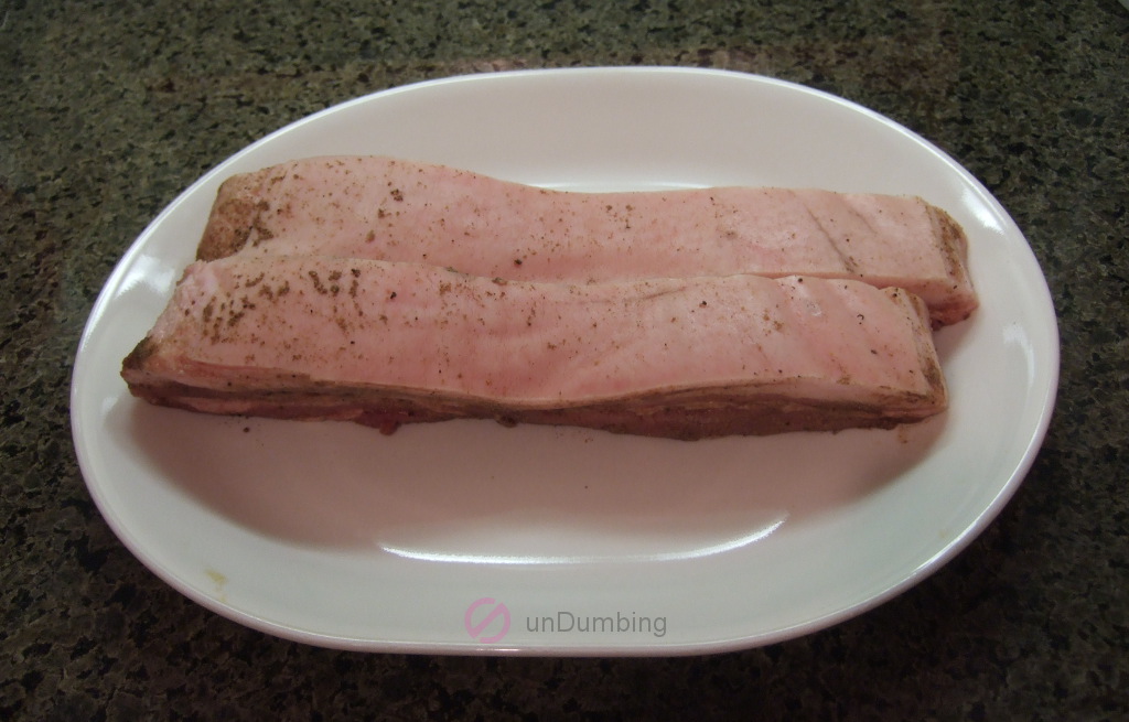 Pork belly with spice rub on a white plate before refrigeration