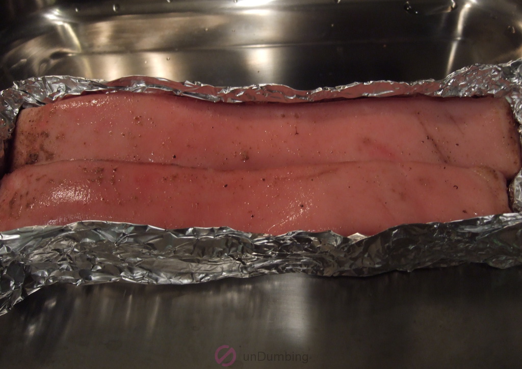 Foil-wrapped pork belly on a roasting pan with vinegar on the skin