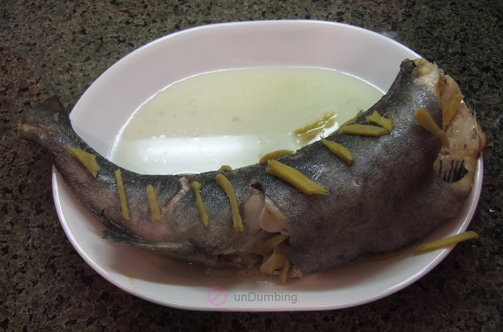 Steamed black cod with ginger strips on a white plate