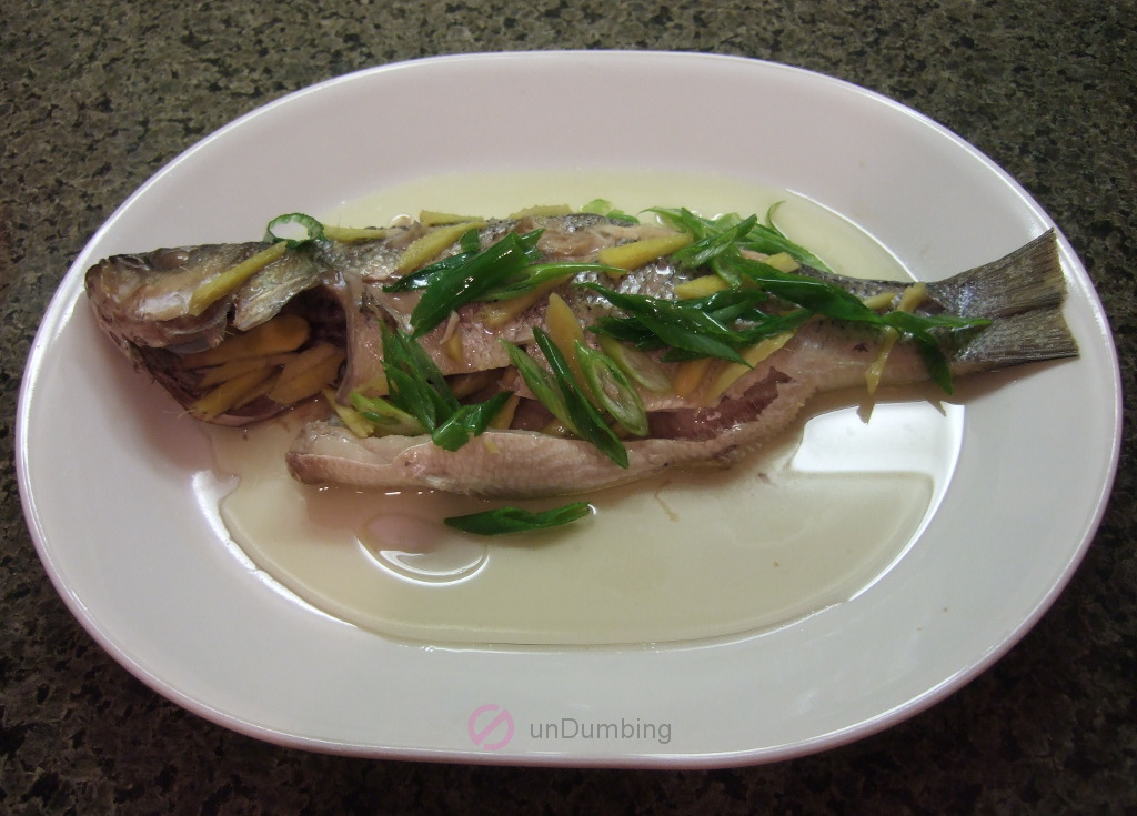 Steamed bass with ginger strips. spring onion strips, and oil on a white plate