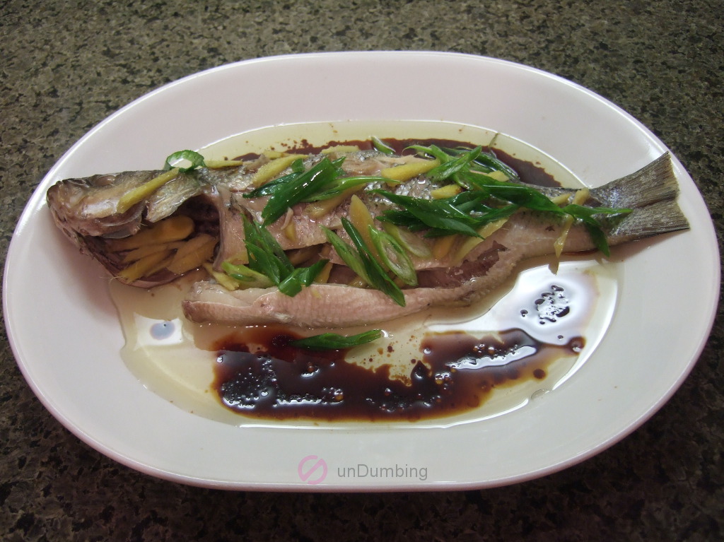 Steamed bass with ginger strips. spring onion strips, oil, and sauce on a white plate