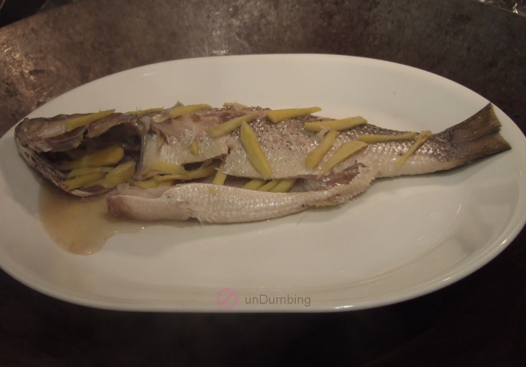 Steamed bass with ginger strips on a white plate in a wok steamer