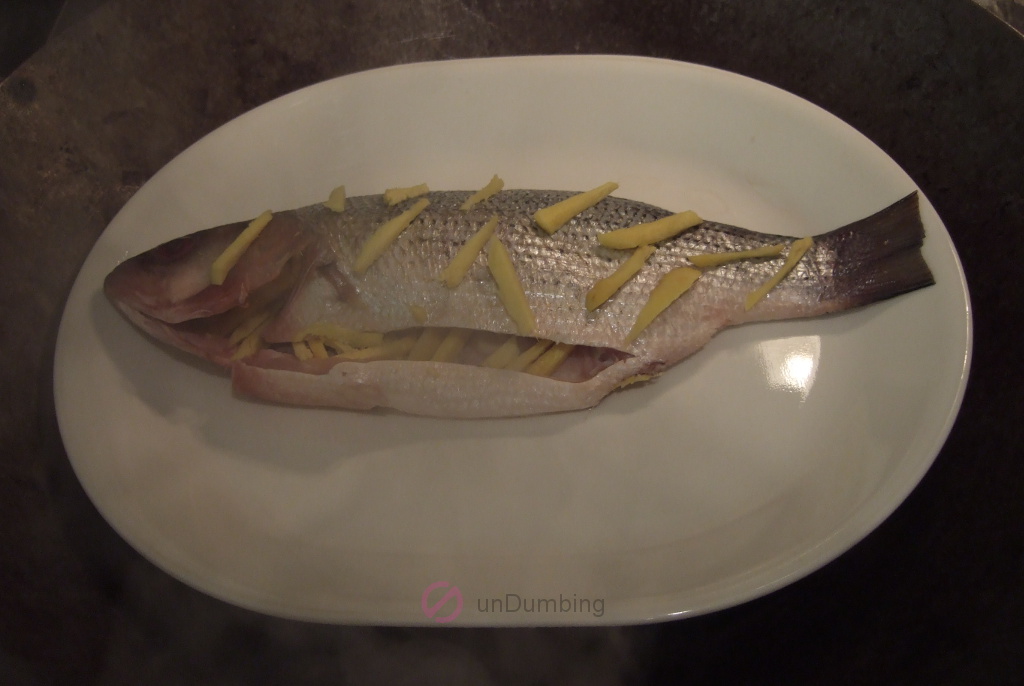 Bass with ginger strips on a white plate in a wok steamer