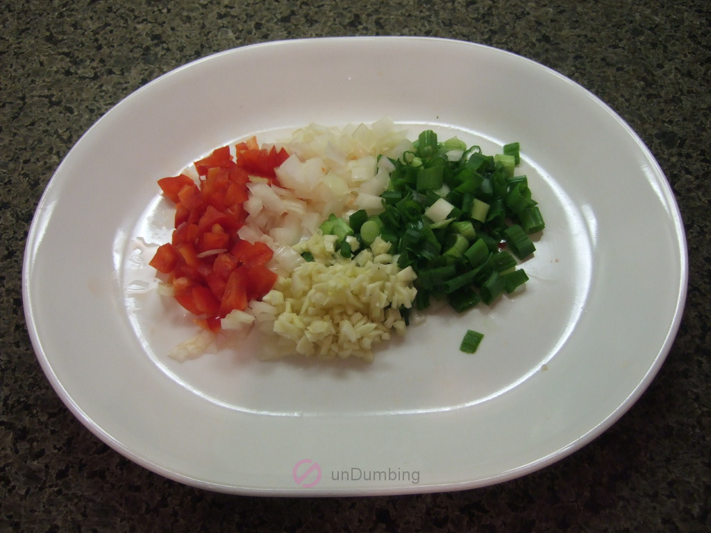 Chopped sweet red pepper, onion, green onions, and, garlic on a white plate