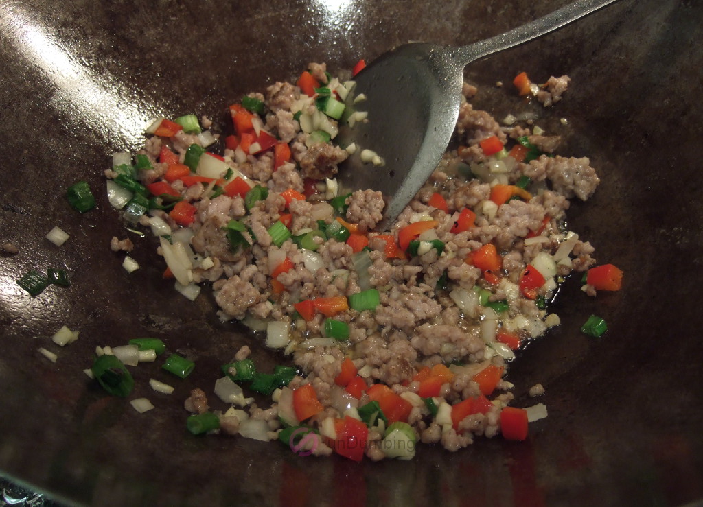 Chopped sweet red pepper, onion, green onions, and, garlic cooked with pork in a wok