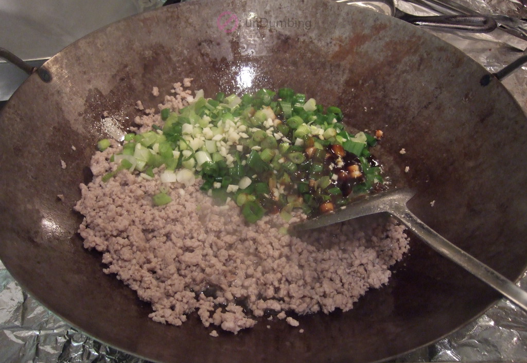 Green onions, garlic, and oyster sauce added to the pork in the wok