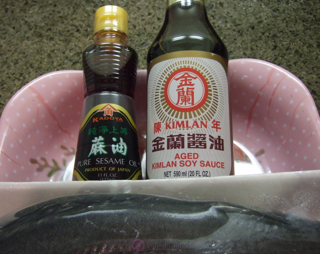 Pink, plastic decorative tray with a new bottle of sesame oil, new bottle of soy sauce, and a white tray of black cod