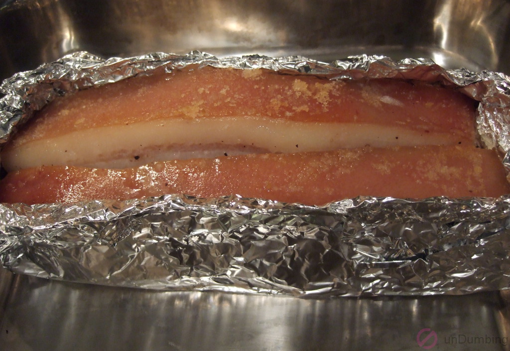 Partially roasted pork belly in a re-tightened foil tray on a roasting pan