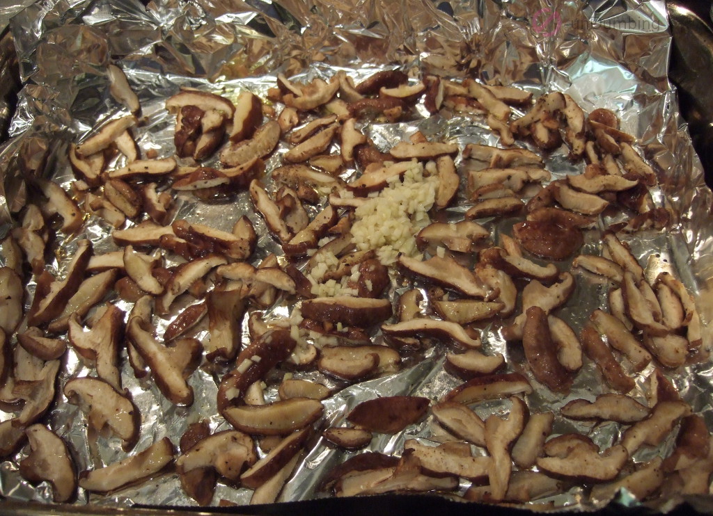 Garlic added to roasted mushrooms on a foil-lined roasting pan