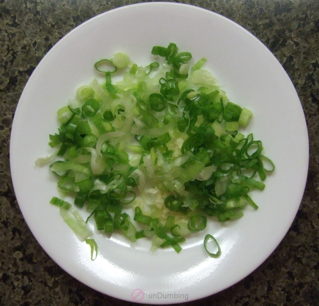 Chopped green onion and minced garlic on a white, round plate