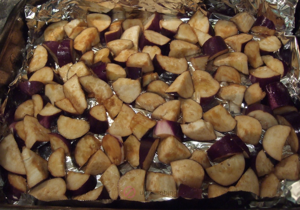 Uncooked eggplants on a foil-lined roasting plan