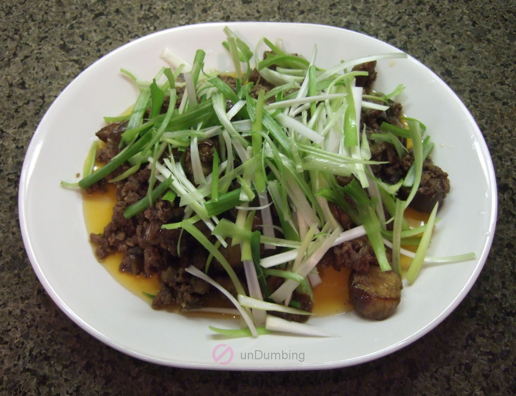 Ground beef and roasted eggplant stir-fry garnished with scallions on a white plate
