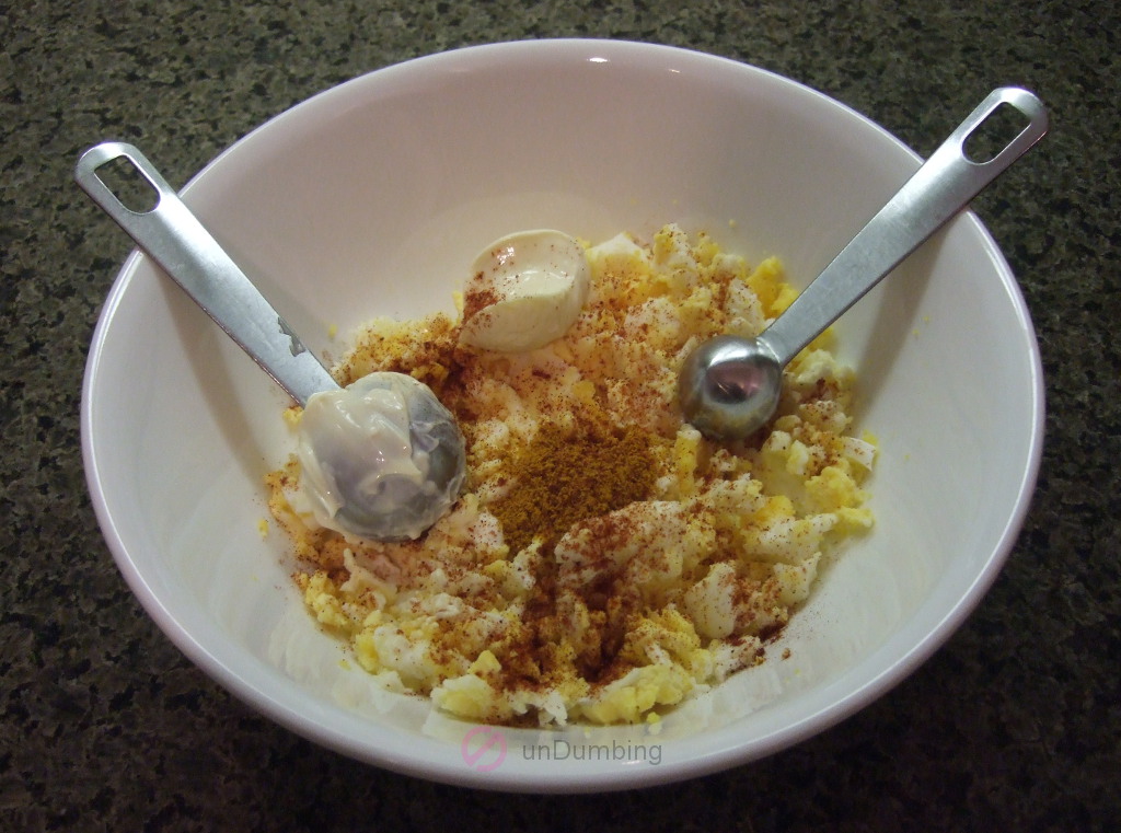 Eggs and seasoning in a white bowl with measuring spoons before mixing