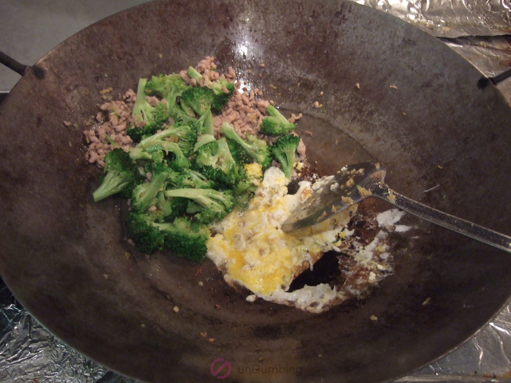 Eggs setting with stir-fried ground pork and broccoli on the side of a wok