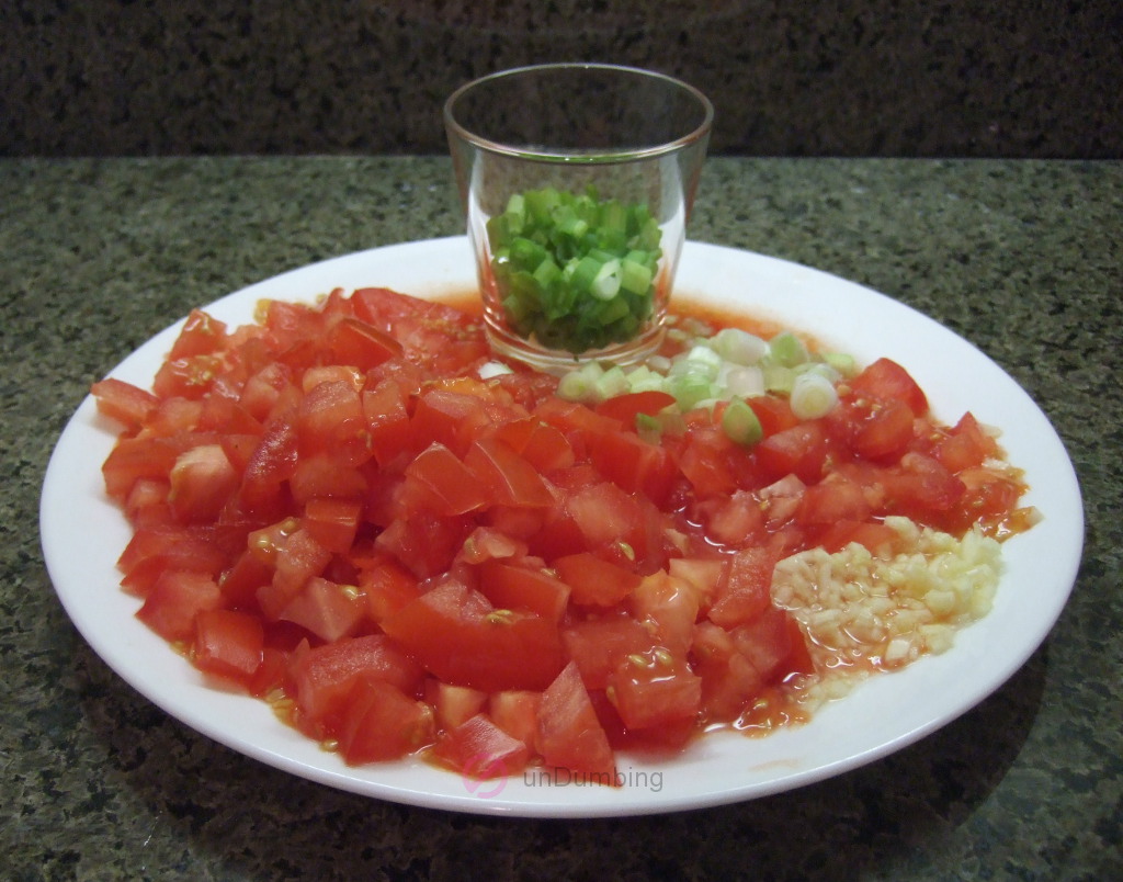 Chopped tomatoes, green onions, and garlic on a white plate; and another shot glass of green onions.