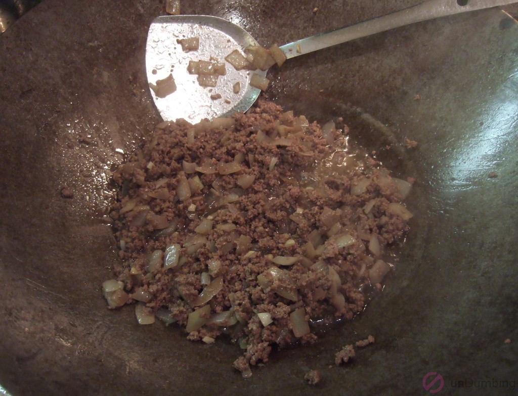 Cooked ground beef in a wok with garlic and onion