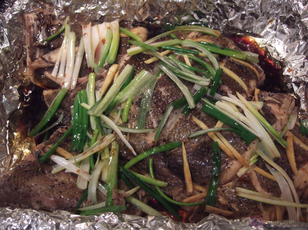 Oil and sauce added to steamed fish on a foil-lined roasting pan