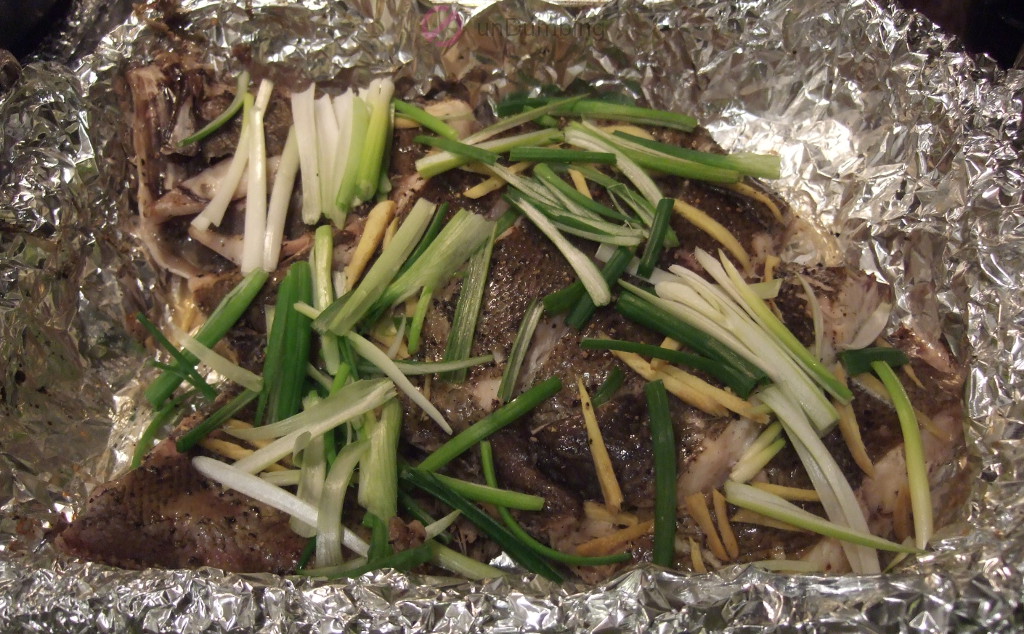 Steamed fish topped with scallions on a foil-lined roasting pan