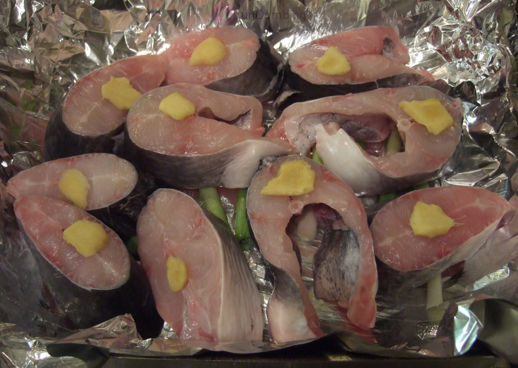 Fish with ginger slices added to the foil-lined roasting pan