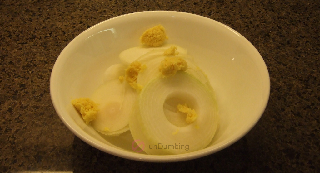 Sliced onion and grated ginger in a white bowl