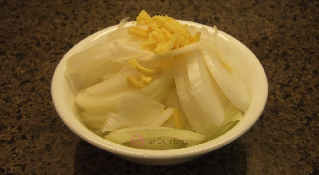 Sliced onion and julienned ginger in a white bowl