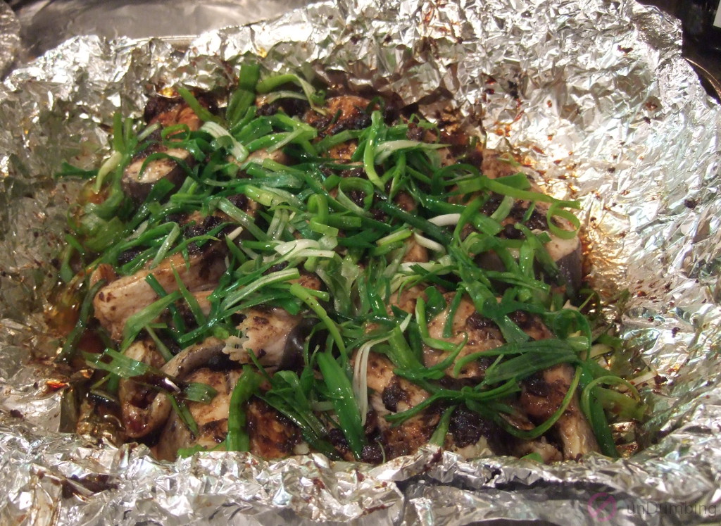 Spring onion, oil, and soy sauce added to the steamed fish in the foil-lined roasting pan