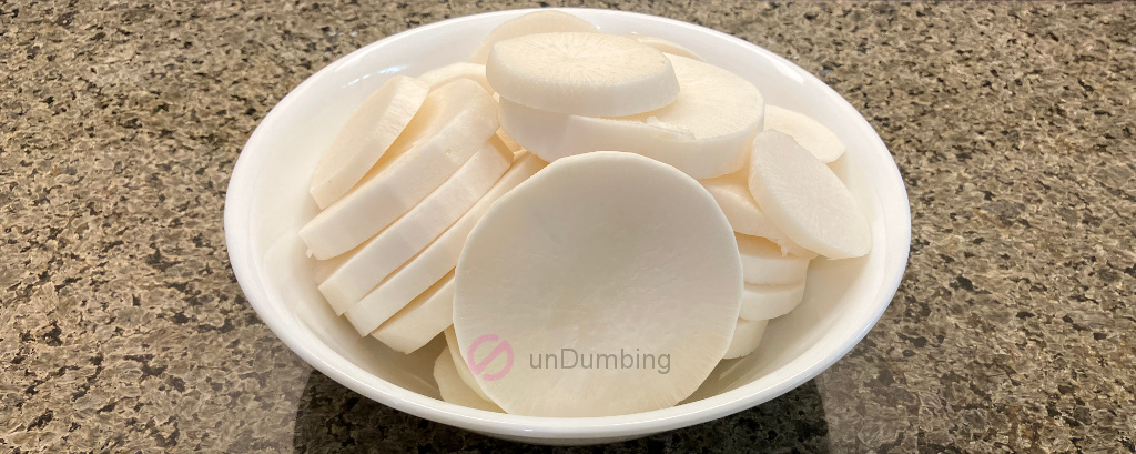 Peeled and sliced radish in a white bowl