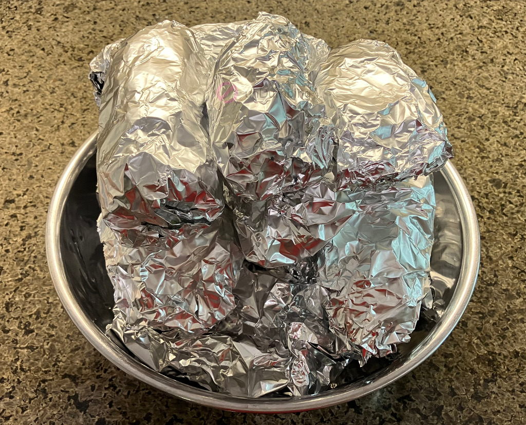 Foil-wrapped bundles of pork wrapped in greens in a stainless steel bowl